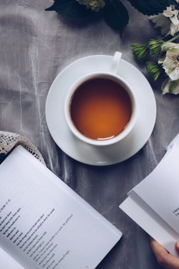 white ceramic teacup with saucer near two books above gray floral textile